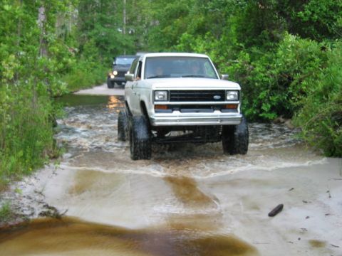 1992 Ford Bronco - A lifted white Ford Ranger drives through a shallow water crossing with another SUV behind it.