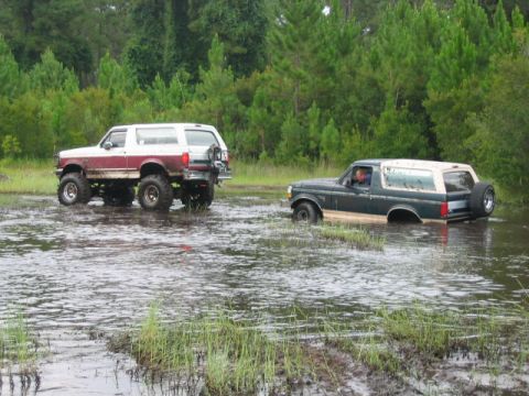 1992 Ford Bronco - Two Ford Broncos navigate a waterlogged field during an off-road event.