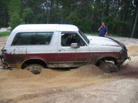 1992 Ford Bronco - A man stands behind a maroon and white Ford Bronco that is stuck in a sandy area with trees in the background.