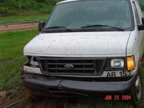 1986 Ford Bronco - A white Ford van sits damaged in a muddy outdoor setting.