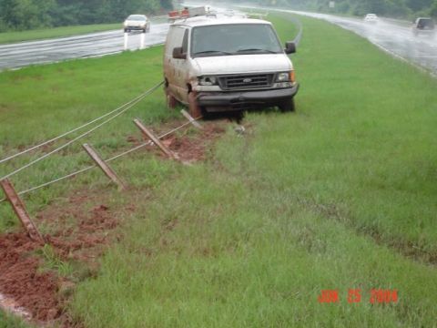 1986 Ford Bronco - A white cargo van has driven off the road and is entangled with fence posts.