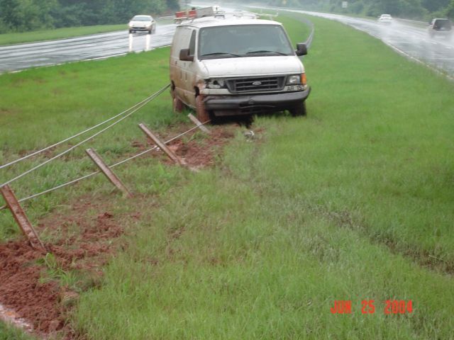 White cargo van off-road, front bumper damaged, pulled by wires attached to fence posts