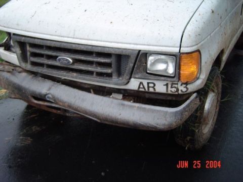 1986 Ford Bronco - Front view of a white van with a damaged bumper and license plate AR 153, seen on a wet surface.