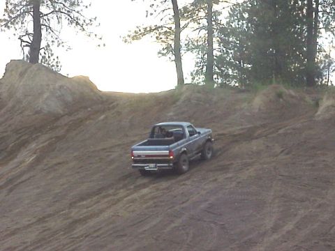 1989 Ford Bronco - A dark blue Ford Bronco navigates a steep dirt incline with trees in the background.
