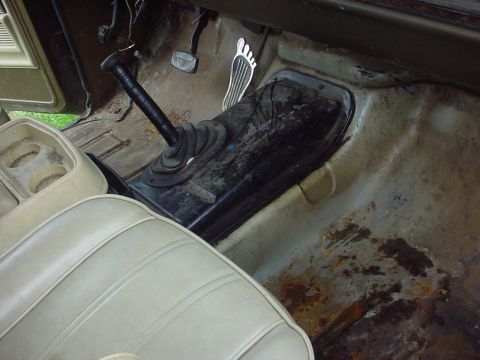1979 Ford Bronco - The interior floor of a vehicle shows a stick shift, pedals, and significant rust damage.