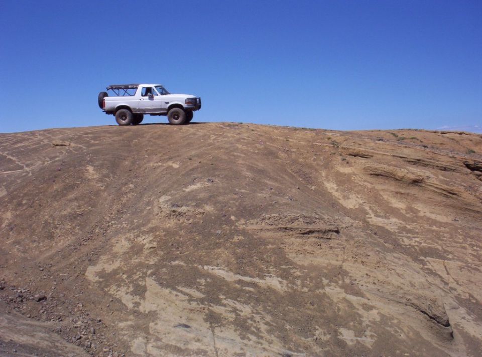 White Ford Bronco perched atop a barren rock dome against a clear blue sky