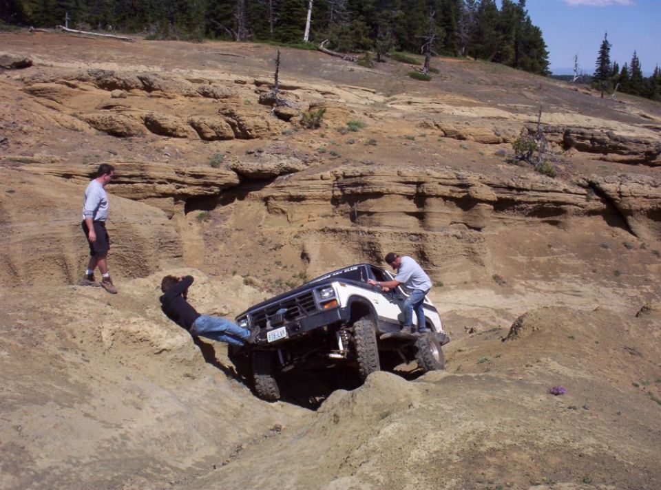 White Bronco climbing out of a rocky pit with two people leaning on it