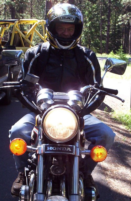 Rider in black leather and full-face helmet seated on a Honda motorcycle on a tree-lined road