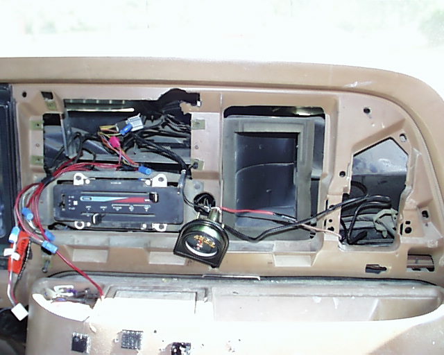 Tan dash center torn apart with exposed wiring, HVAC slider controls and an added round gauge