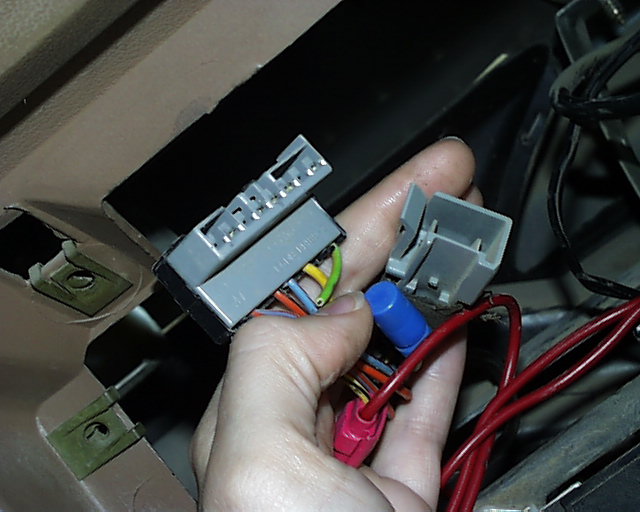 Hand holding gray factory radio connectors and spliced wiring at an open dash