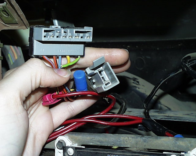 Hand holding gray stereo wiring harness plug with crimped connectors