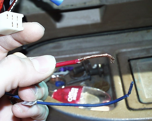 Hand holding a stripped red wire and white connector during vehicle wiring work