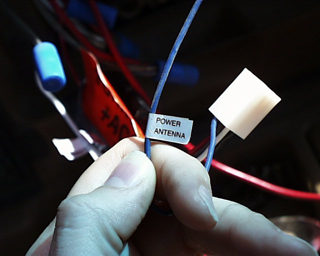 Hand holding blue wire labeled POWER ANTENNA during car stereo wiring install