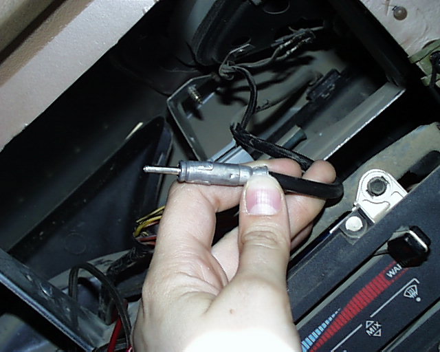 Hand holding a test light probe over a torn-apart dash with HVAC slider controls