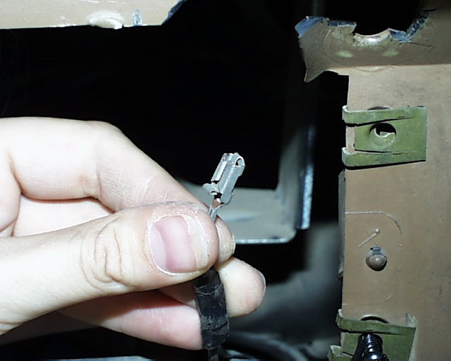 Hand holding a small two-pin electrical connector inside a stripped vehicle body cavity