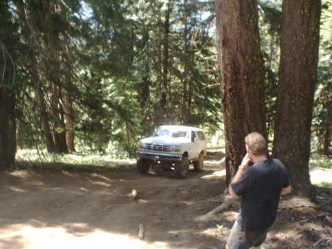 1978 Ford Bronco - A white 1992 Ford Bronco navigates a wooded trail, with a man observing the scene.