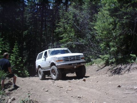 1978 Ford Bronco - A lifted white Ford Bronco navigates a rough, wooded trail.