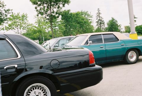 1998 Ford Crown Victoria - A teal sedan with a vinyl roof is parked next to a black sedan, showing their rear quarter panels.