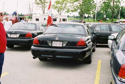1998 Ford Crown Victoria - Multiple black Ford Crown Victoria police cars are parked in a lot on a sunny day.