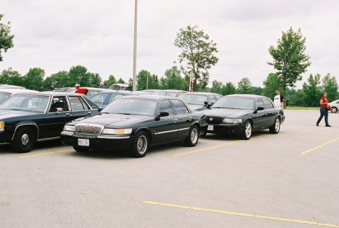 1998 Ford Crown Victoria - Two black sedans, one identified as a 1998 Ford Crown Victoria, are parked in an outdoor lot.