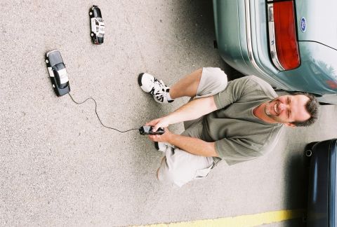 1998 Ford Crown Victoria - A man crouches down to play with two remote control cars, one of which is a police car replica.