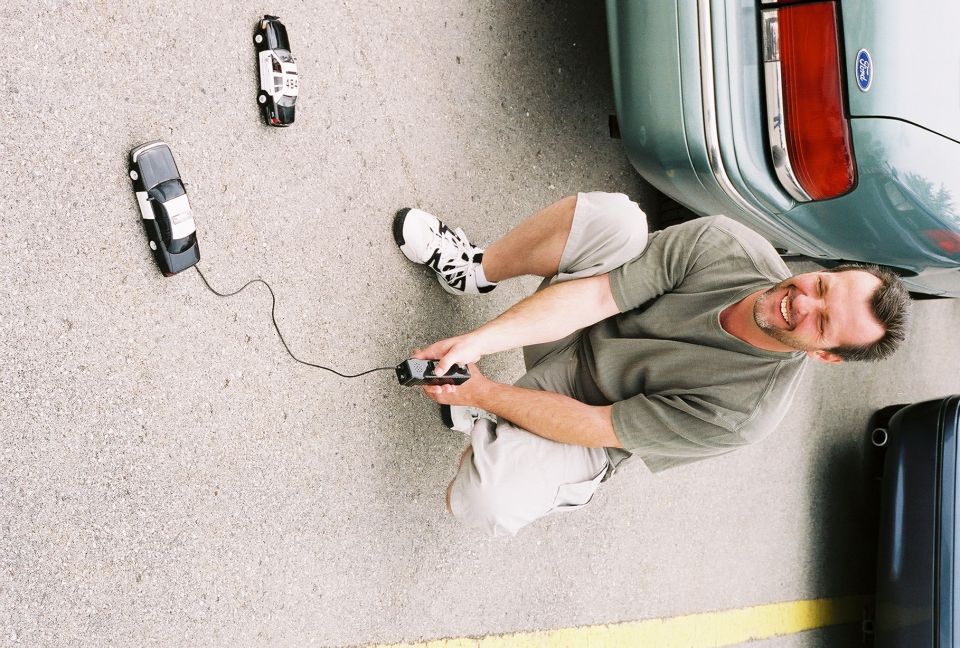 Man playing with remote control cars next to a real car