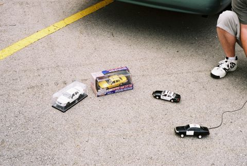 1998 Ford Crown Victoria - Several toy vehicles, including a police car and a taxi, are arranged on a paved surface.