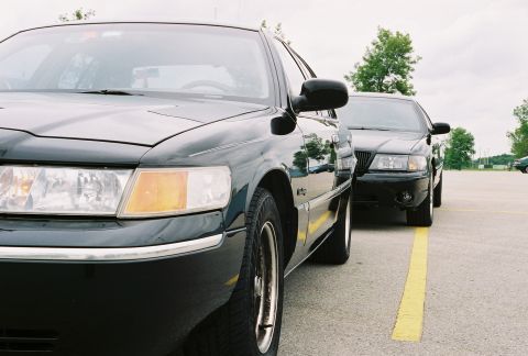 1998 Ford Crown Victoria - Two black sedans, one a 1998 Ford Crown Victoria, are parked side-by-side in a lot.