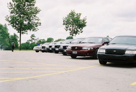 1998 Ford Crown Victoria - A line of Ford Crown Victoria Police Interceptors are parked in a lot under a cloudy sky.