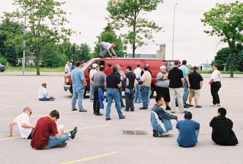 1998 Ford Crown Victoria - A group of people are gathered in a parking lot around a red van.