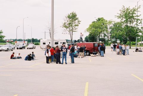 1998 Ford Crown Victoria - A group of people are congregated in a parking lot, with a red van and other vehicles present.