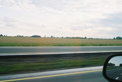 1998 Ford Crown Victoria - A view from a vehicle shows a highway and distant cars reflected in the side mirror.