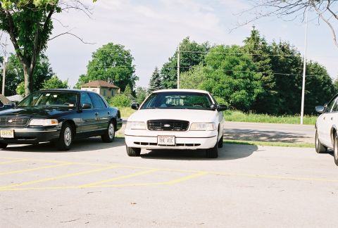 1998 Ford Crown Victoria - A white 1998 Ford Crown Victoria is parked in a lot, displaying a custom license plate that reads "THE VIC".