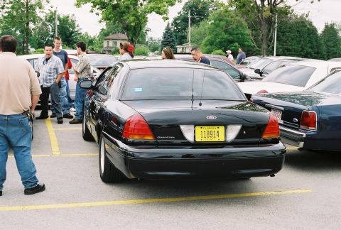 1998 Ford Crown Victoria - A black 1998 Ford Crown Victoria is parked in a lot with other vehicles and people around.