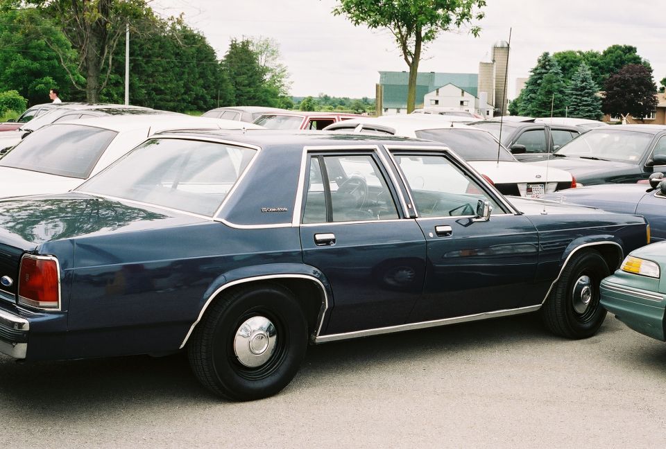 Dark blue sedan parked in a lot, side view. Other cars are visible around it