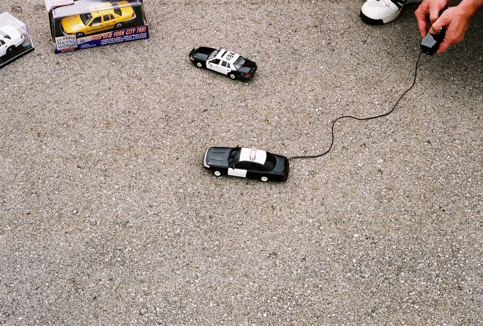 Toy police car on asphalt, connected by wire to a remote control
