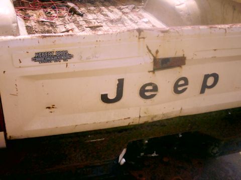 1980 Ford Bronco - Rear view of a white Jeep pickup truck showing the tailgate and a dealer sticker.