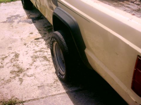 1980 Ford Bronco - The side profile of a Jeep Comanche pickup truck is visible, with a focus on the rear wheel and fender area.