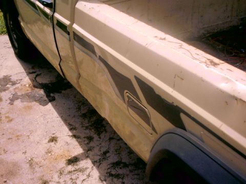 1980 Ford Bronco - This beige pickup truck features a dark stripe graphic along its side, with visible signs of wear and tear.