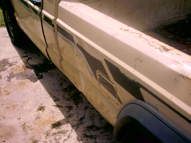 Side view of beige pickup truck bed with dark stripe graphic and visible rust