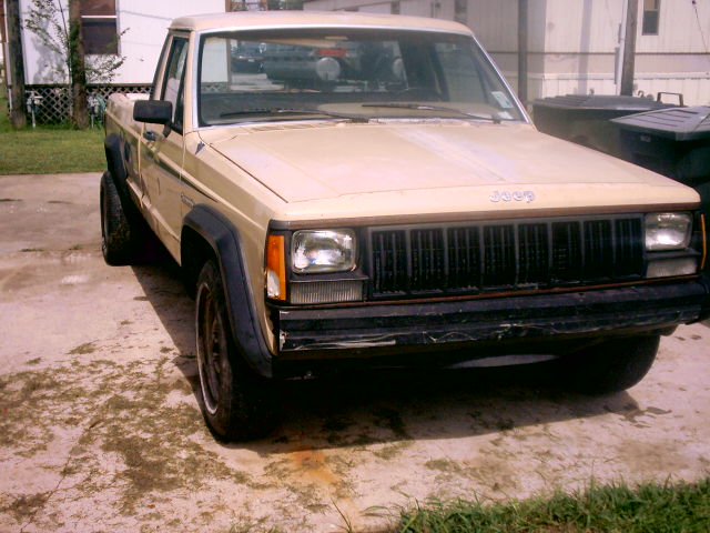 Tan Jeep Comanche pickup truck, 3/4 front view. Visible 'Jeep' badging on grille