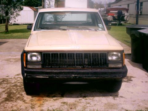 1980 Ford Bronco - A tan Jeep Comanche pickup truck is parked outside on a concrete driveway.