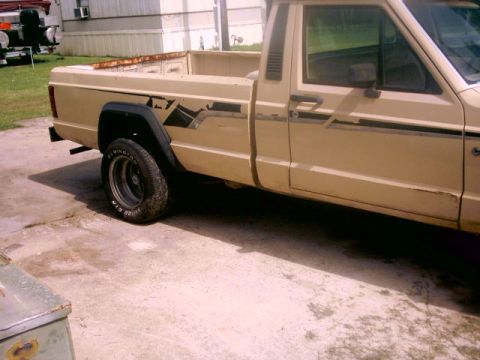 1980 Ford Bronco - Tan pickup truck with black fender flares and side graphics is parked on a concrete surface.