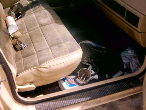 1980 Ford Bronco - Vehicle interior with a worn seat and debris on the floor, including cleaning supplies and automotive parts.