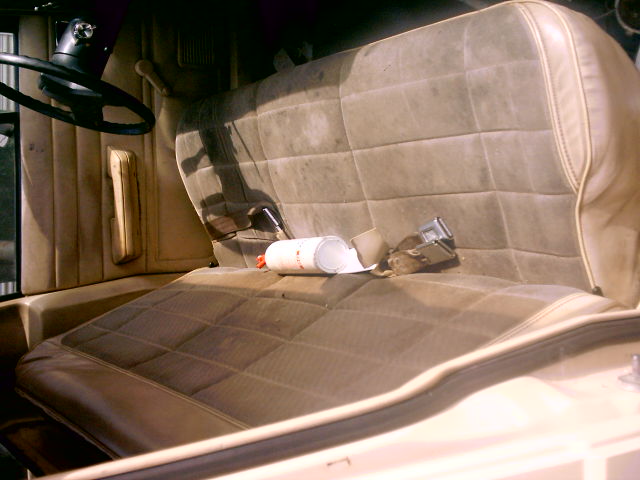 Interior shot of a vehicle's front bench seat, showing worn upholstery and a seatbelt. A white can is on the seat