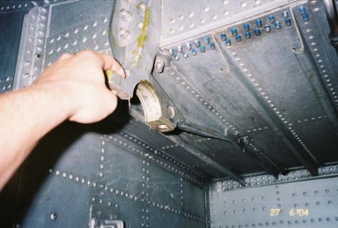 1988 Ford Bronco - A hand interacts with a metal bracket inside a heavily riveted compartment.
