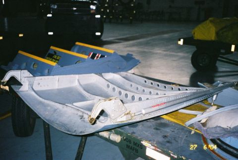 1988 Ford Bronco - An unidentified aircraft component is displayed on a workbench, with a dark vehicle visible in the background.