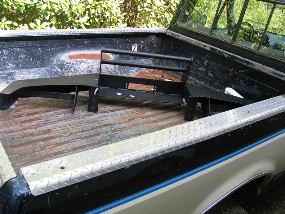 Truck bed with a black aftermarket bumper and brush guard loaded inside. The truck has a diamond plate bed rail