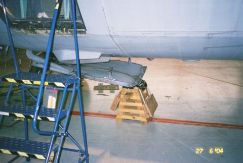 1988 Ford Bronco - The underside of an aircraft is shown, elevated on wooden supports, with a blue rolling ladder positioned to the left.