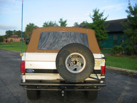 1992 Ford Bronco - Rear view of a white Ford Bronco with a brown soft top and a spare tire mounted on the back.